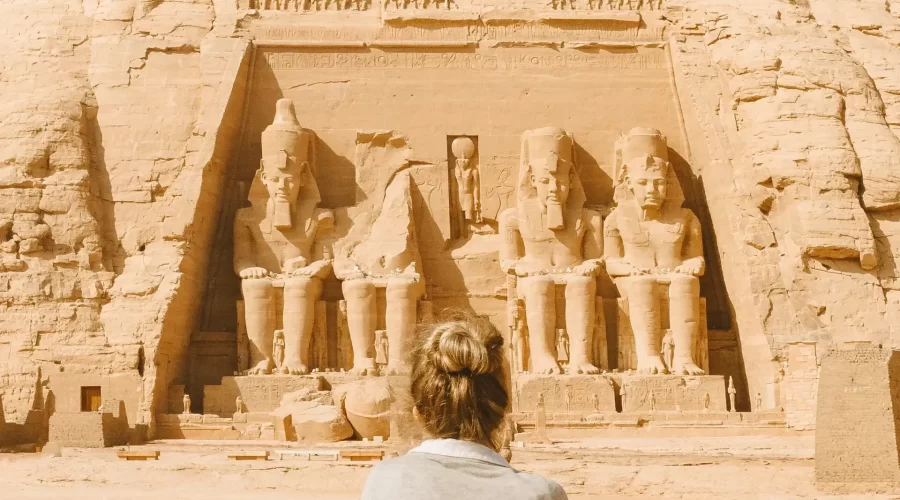 Visitante admirando la fachada de El Templo de Abu Simbel y las estatuas colosales de Ramsés II en Egipto.